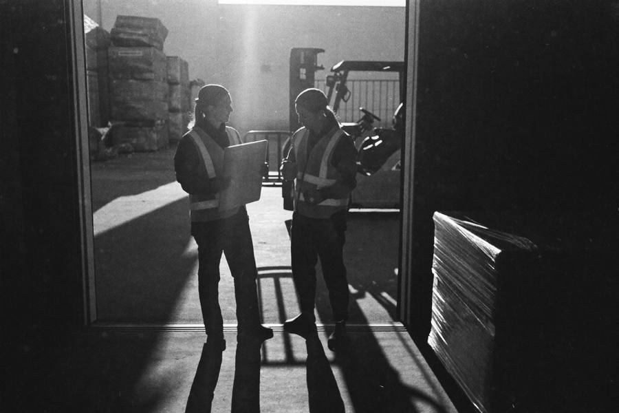 A clipboard passing between two workers at a warehouse dock during shift change